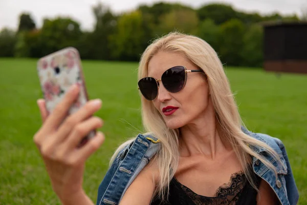 Bir kız güzel bir ormanın arkasında fotokromik gözlük alanında telefonda fotoğraf çeker.