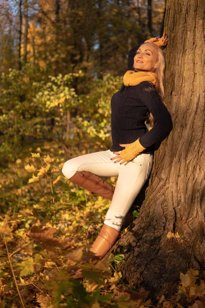 La chica descansa en un árbol y es fotografiada al atardecer con ropa de vaquero, botas marrones pierna en un árbol cara a cara — Foto de Stock