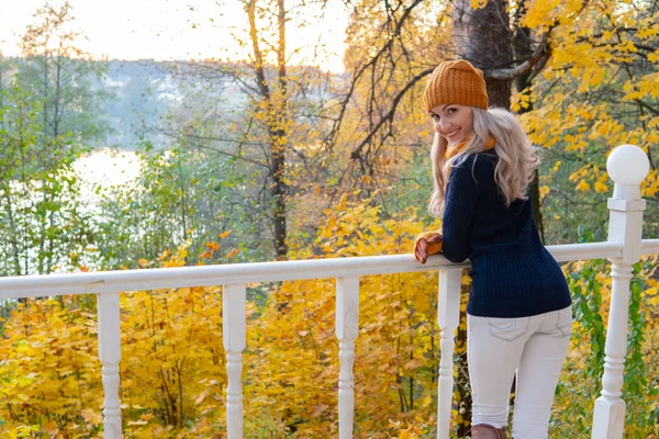 秋の森の女の子が白い橋の端に立ち、明るい黄色の葉で川を見る — ストック写真
