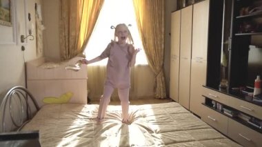 Kız dans ediyor ve yatağa düşüyor eğleniyor ve ellerini sallıyor. Aydınlık bir odada ve bir peçetede.