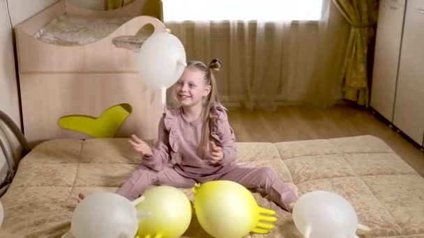 Jovem alegre joga com bolas em luvas em uma bela casa em uma grande cama bonita com bolas enormes e belas bolas brancas grandes. em um quarto bege . — Vídeo de Stock