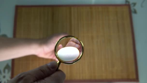 Guarda l'uovo sotto la lente d'ingrandimento vista sfondo sfocato dall'alto, sfondo marrone sul tavolo — Video Stock