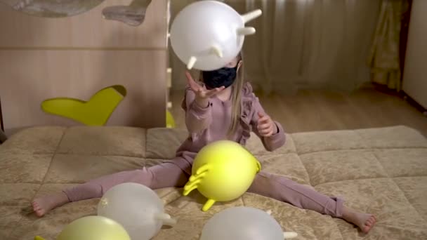 Genieten van meisje spelen met ballen in handschoenen in een mooi huis op een groot mooi bed met gele handschoenen en mooie grote witte ballen. in een lichte kamer. het masker — Stockvideo