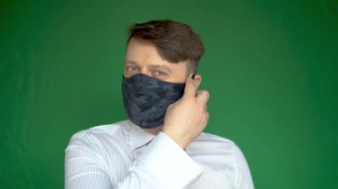 Mutlu, olgun bir adam maskesini çıkarır ve yeşil bir arka planda güler yüzle güler.