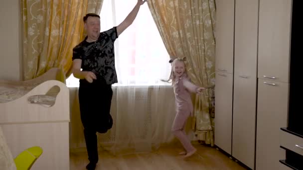 Un vieux papa joyeux danse avec une fille joyeuse briquet dans un grand salon en vêtements à la mode. Sur contre une fenêtre lumineuse . — Video