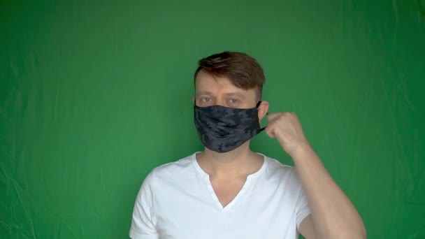 Glad ung man tar av masken från huvudet och ler med en bra look bakgrund grön ljust dagsljus klarblå ögon — Stockvideo