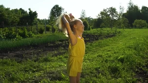 Menina feliz endireita o cabelo, jovem olha para a câmera emoções positivas conceito feliz de bem-estar contra o céu azul e grama verde em férias. Verão na natureza — Vídeo de Stock