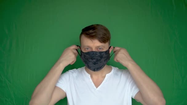 Onvoorzichtige volwassen man neemt het masker van zijn hoofd en verheugt zich met mooie ogen op een groene achtergrond met daglicht donker masker blauwe ogen — Stockvideo