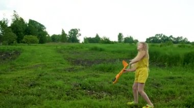 Bir kız gökyüzüne bir uçak fırlatır yeşil çimenlerin ve mavi gökyüzünün arka planına karşı köyde uzun sarı saçlı bir kız. Doğada yaz