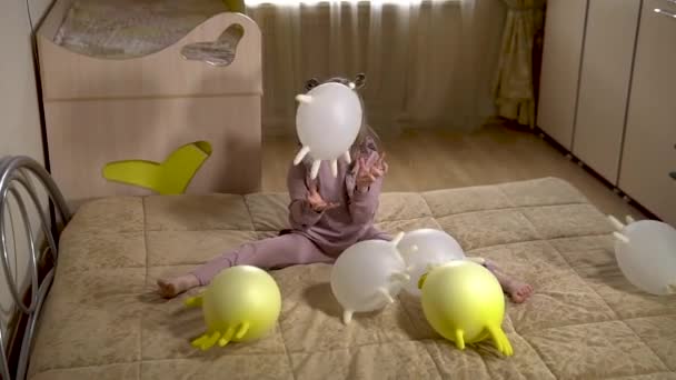 Meisje schoolmeisje genieten van het spelen van handschoenen met ballonnen in een kinderkamer op een zachte bank met gele handschoenen en witte ballonnen. in een zonnige kamer. — Stockvideo