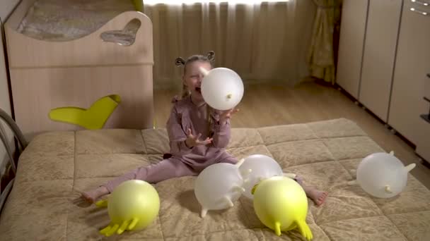 Una colegiala feliz juega con globos con guantes en una hermosa casa en un sofá suave con enormes bolas y hermosas bolas blancas grandes. en una habitación soleada . — Vídeo de stock