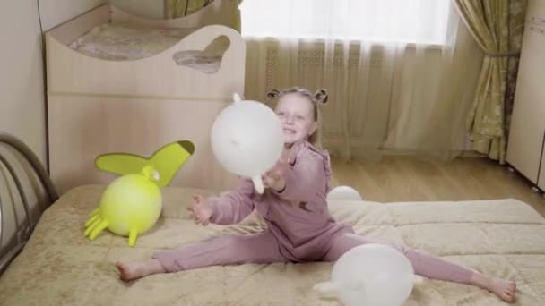 Joyeuse écolière joue avec des ballons dans des gants dans un bel appartement sur un beau lit avec des gants jaunes et des boules blanches. dans une chambre beige. — Video