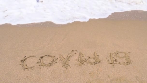 Covid weggespoeld door water in de oceaan door blauwe golf, de inscriptie van het zand wordt weggespoeld — Stockvideo