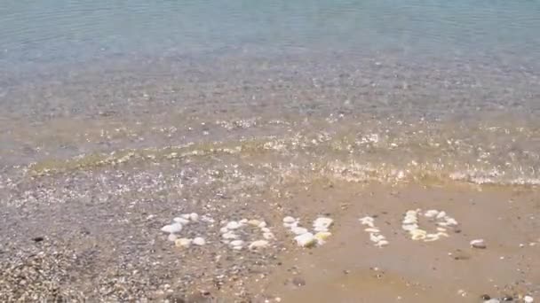 Ковид смывается волной из океана, надпись сделана из камней, холодная вода смывает надпись на воде из гальки — стоковое видео