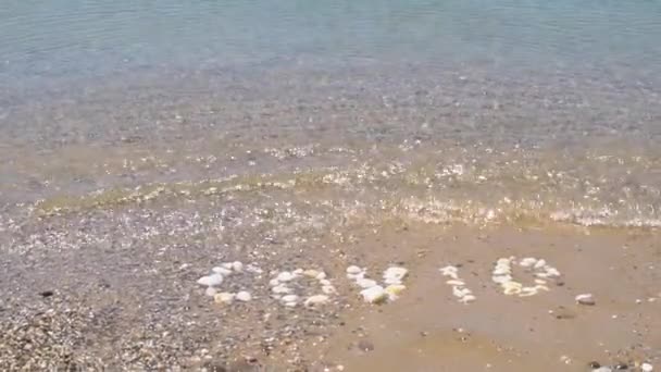 Covid lavado por uma onda do oceano, a inscrição é feita de pedras, água fria lava a inscrição na água de seixos — Vídeo de Stock