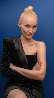 Uğurlu büyük kız kameraya poz veriyor, siyah takım elbiseli, mavi arka planda Avrupalı bir yüzü olan beyaz bir gün ışığında. Göstergeler