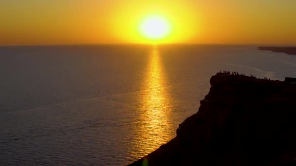 夏夜，夕阳西下的海面上，悬崖上的橘红色的灯光，缓缓地拍下了大海的景象 — 图库视频影像