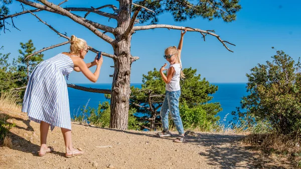 Una donna fotografa il suo bambino sul mare contro un albero — Foto Stock