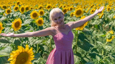 Güneş gözlüklü kırmızı kareli bir elbise içinde, yaz sıcağında güzel bir sarışın, parlak Avrupalı görünümlü.