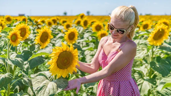 Donna in girasoli in un bellissimo vestito rosso in occhiali da sole, bella bionda nel calore dell'estate luce brillante — Foto Stock