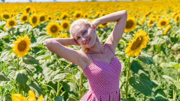 Donna in girasoli in un bellissimo vestito rosso in occhiali da sole, una bella bionda nel caldo dell'estate il sole splende. — Foto Stock