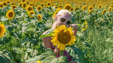 Güneş gözlüklü, kırmızı elbiseli, yaz sıcağında sarışın, açık renk saçlı bir kadın.