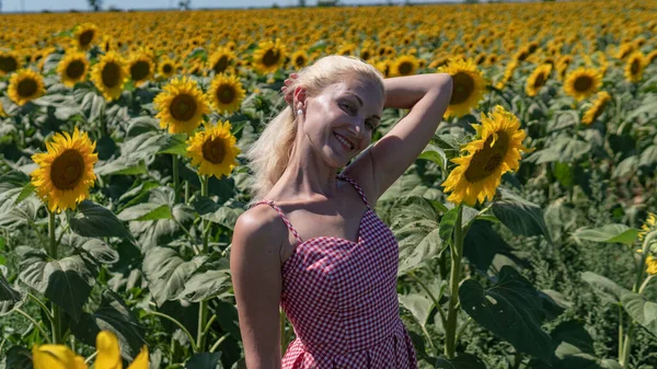 Ragazza in girasoli in un abito rosso con gli occhiali da sole, una bella bionda nel caldo dell'estate, il sole splende aspetto caucasico — Foto Stock