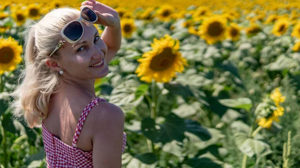 Ragazza in girasoli in un vestito rosso in occhiali da sole, bella bionda nel calore dell'estate luce brillante — Foto Stock