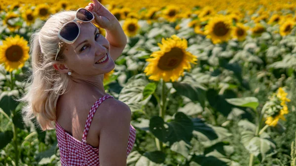 In girasoli in un vestito rosso in occhiali da sole, una bella bionda nel caldo dell'estate il sole splende aspetto europeo — Foto Stock