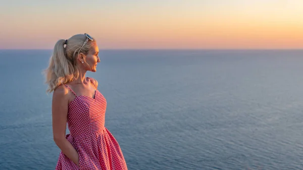 Una bella ragazza adulta con un aspetto caucasico guarda il tramonto con la schiena in estate la sera — Foto Stock