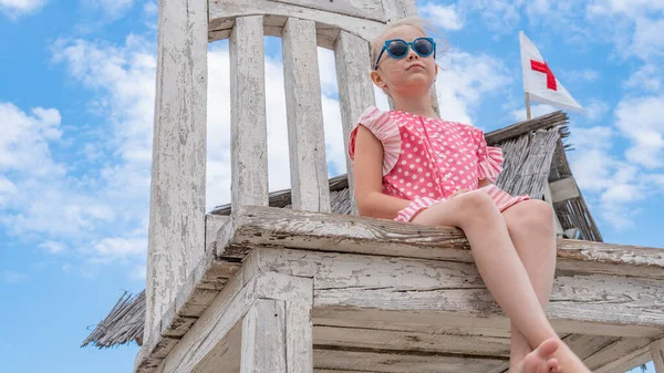 La ragazza si siede su una sedia enorme immagine dal basso, indossando occhiali da sole, in estate con nuvole blu — Foto Stock