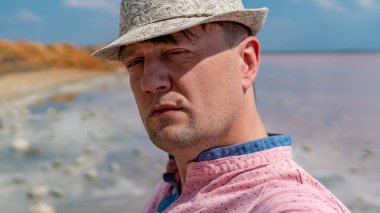 Denizde şapkalı bir adam ve pembe gömlekli yaşlı bir adam denizdeki güneşten burunlarını çekmiş kameraya bakıyor.