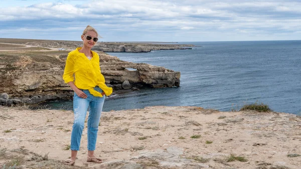 Ragazza si erge su rocce simili a un coccodrillo in mare, camicia gialla — Foto Stock