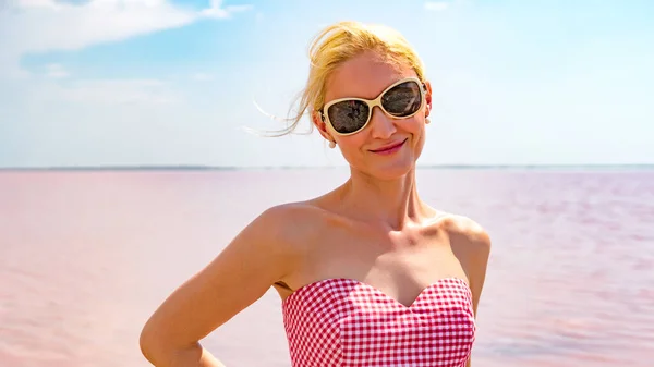 Donna sorridente in un bel vestito con un bel sorriso sullo sfondo di un lago rosa durante il giorno e l'estate — Foto Stock