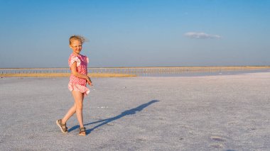 Güzel elbiseli genç bir bayan. Güzel bir gülüşü var. Gün boyunca ve yaz boyunca bir tuz gölünün arka planında.