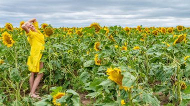 Sarı yetişkin elbiseli güzel kadın sıcak güneşli havada kameraya gülümsüyor.