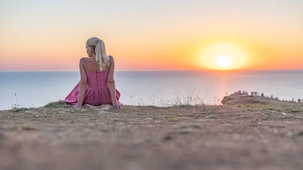 Una chica adulta alegre con una apariencia caucásica mira la puesta de sol con su espalda en el verano por la noche —  Fotos de Stock
