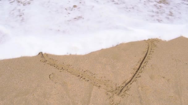Rysunek serca zmytego wodą, fala z morza, napis zrobiony palcem, zimna woda zmywa napis z piasku latem słonecznym — Wideo stockowe