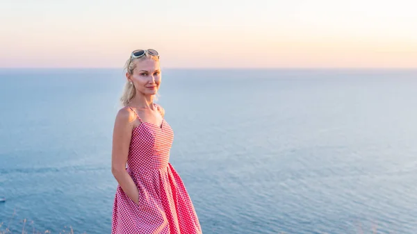 Una bella ragazza adulta con un sorriso perfetto guarda il tramonto si alza al sole con il viso la sera d'estate — Foto Stock