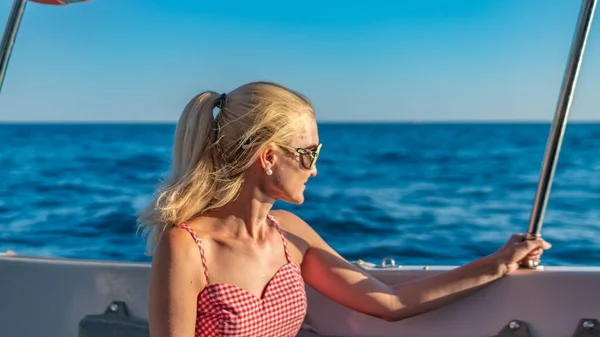 Donna allegra siede su uno yacht, con le labbra tenere intorno al mare, il concetto di vita urbana in bicchieri monocromatici durante il giorno — Foto Stock