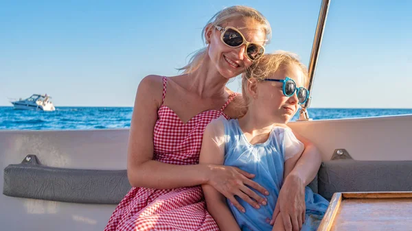 Chica feliz se sienta en un yate, un joven sonriendo en la cámara en el horizonte del mar, el concepto de bienestar en gafas monocromas en el verano, mamá y su hija —  Fotos de Stock