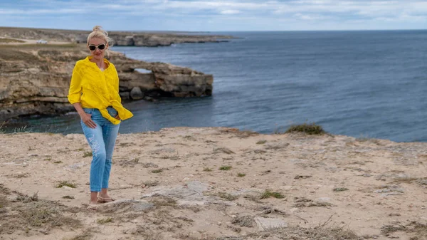 Felice signora in camicia gialla giovane con un look gentile nuvole blu durante il giorno e in estate su una spiaggia rocciosa — Foto Stock