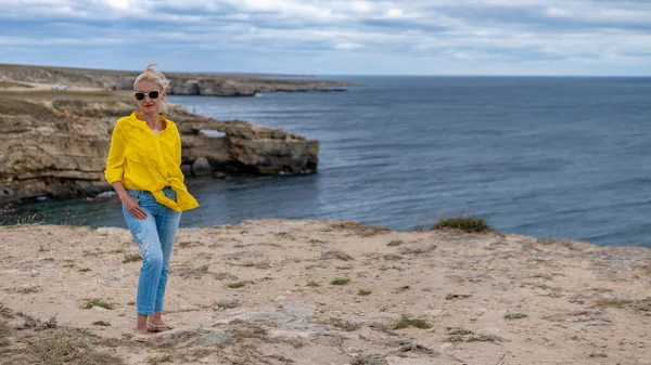 Bella signora in camicia gialla giovane con labbra tenere nel caldo sole su una spiaggia rocciosa — Foto Stock