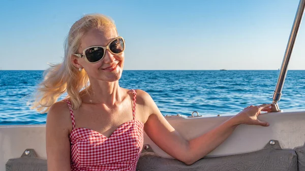 Donna sorridente seduta su yacht, con uno sguardo gentile intorno al mare, concetto di attività webinar in occhiali da sole in estate — Foto Stock