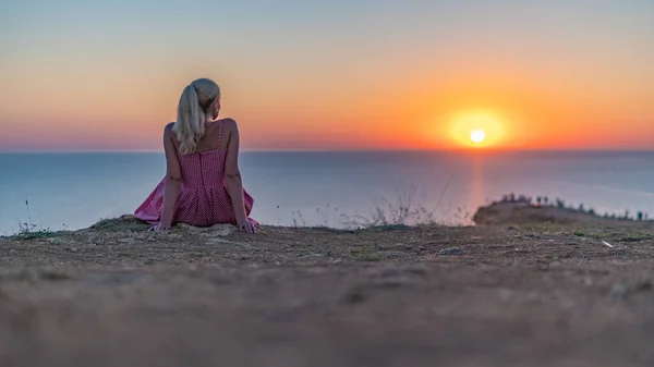 La ragazza è seduta con le spalle a noi sullo sfondo del tramonto, guardando il sole la sera d'estate — Foto Stock