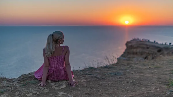 Felice giovane donna con un aspetto eccellente guarda il tramonto siede con la schiena in estate la sera siede — Foto Stock