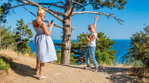 Madre e figlia posano nei boschi con vista sul mare in estate nel caldo in occhiali da sole, in vacanza vengono fotografati su uno smartphone — Foto Stock