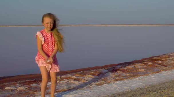 Una chica en un lago salado derrama sal, se regocija y sonríe — Vídeos de Stock