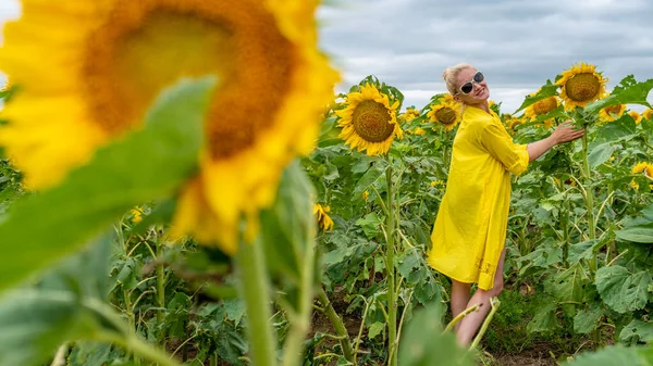 夏の日にひまわりと畑の背景に若い黄色のドレスの笑顔の女の子 — ストック写真