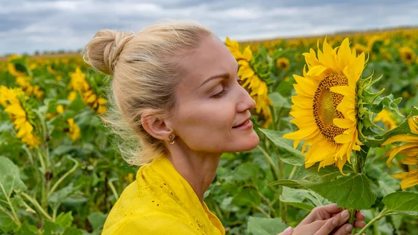 夏の日に青い雲とひまわり畑の背景に柔らかい唇を持つ黄色のドレスの大人の美しい女性 — ストック写真